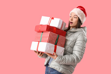 Young woman in Santa hat with Christmas gifts on pink background