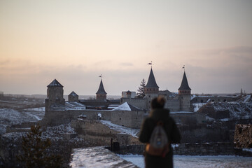 Beautiful girl looks at the historical castle at sunset in Ukraine. The city of Kamianets-Podilskyi.