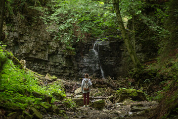A beautiful girl looks at a waterfall in the forest