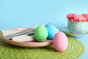 Beautiful festive table setting for Easter with colorful eggs and flowers on blue background