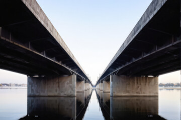 Symmetrical underbelly view of a modern concrete bridge, highlighting the architectural design and reflections on the water below, emphasizing structure and symmetry. Generative AI
