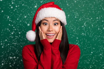 Closeup photo of young korean woman wear red pullover nice santa claus hat touch cheeks shock black friday sale isolated on green color background