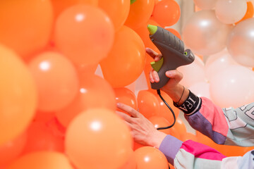 Making orange balloon arch decorations for Halloween or birthday party. Hand with a glue gun.