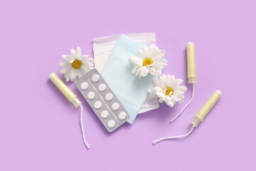 Menstrual pads with tampons, pills and chamomile flowers on purple background