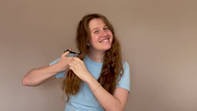 young woman with long red or light brown hair cuts off his hair and smiling at camera, concept haircut, split ends