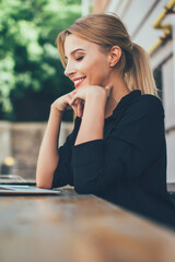 Obraz premium Side view of happy hipster girl watching positive comedy movie on content website connected to public wifi on laptop device, positive female blogger enjoying online video chatting with followers