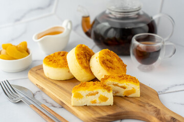 Three soft cheesecakes topped with golden crumble served on a wooden board with tea and peach slices. Concept of a sweet dessert, teatime, and homemade baking.