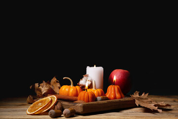 Burning candles with pumpkins, apple, cinnamon, dried orange, acorns and autumn leaves on wooden...