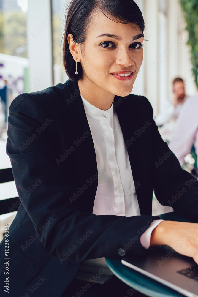 Poster portrait of positive businesswoman updating software on laptop while doing remote job in cafe interi