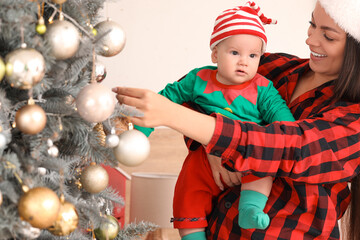 Mother and her little baby dressed as elf near Christmas tree in bedroom