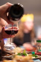 A glass of red wine being filled from a bottle over a family dinner during the holiday season portrait view.