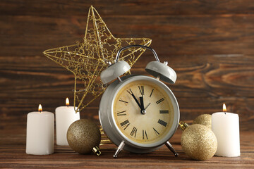 Alarm clock, burning candles, Christmas balls and star on table against wooden background