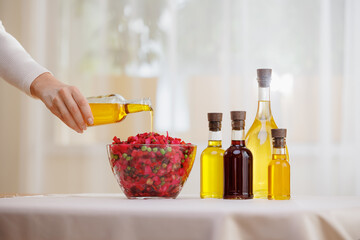 Woman hold glasses bottle with fresh extra virgin, sunflower oil pouring into bowl of vinaigrette...