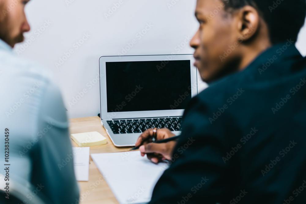 Poster back view of two businessmen discussing strategy for opening new office of company while modern lapt