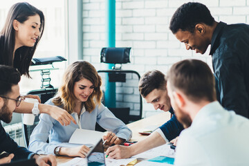 Fototapeta premium Successful group of male and female business analytics analyzing strategy for startup project during collaborating indoors, positive smiling colleagues enjoying cooperating near office desktop