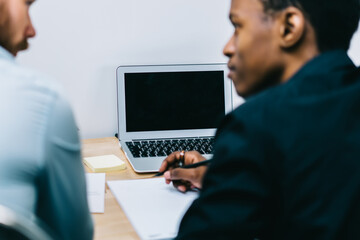 Back view of two businessmen discussing strategy for opening new office of company while modern laptop computer with blank screen area for advertising your internet advertising staying on table