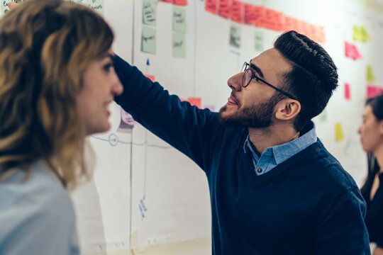 Group of young multicultural perspective managers creating idea of strategy for productive work of company, curiosity male expert in optical spectacles reading interesting note from sticks on wall