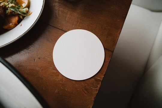 White coaster in a restaurant: Clean and blank, perfect for showcasing a beverage or brand. Ideal for use in pubs, bars, or cafes to enhance dining and drinking experience