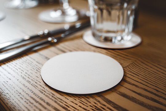 A white circle beer coaster mockup placed on a rustic wooden table.