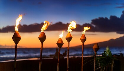 Multiple tiki torch with flame burning on the beach with a dramatic sunset in the background; tiki torch burning during sunset by the beach; beautiful resort by the ocean with tiki torches with flames