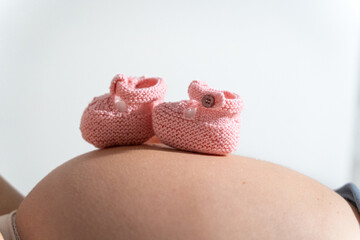 Close-up of pink knitted baby booties placed on a pregnant woman's belly, set against a plain white background. Perfect for themes of pregnancy, anticipation, and baby preparation.