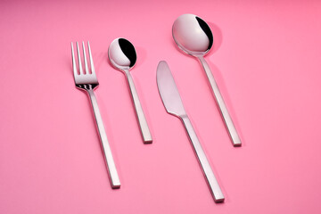 fork and knife and spoons on pink background