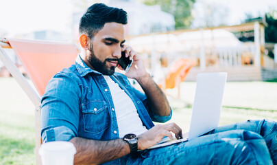 Serious Spanish freelancer in casual wear calling to operator service for consultancy about online problem with wireless connection on laptop computer, young man using international internet