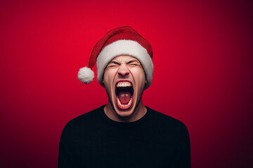 Excited young man wearing Santa hat screaming with joy on red background. Fun and energetic...