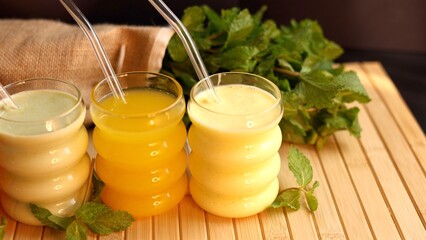  Drinks in orange, green, yellow, and creamy tones with clear straws sit on wooden surface. Scene promotes fresh, healthy beverages for light, energizing refreshment.