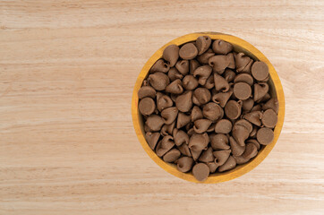 Overhead view of a bowl filled with milk chocolate chips on a wood tabletop.
