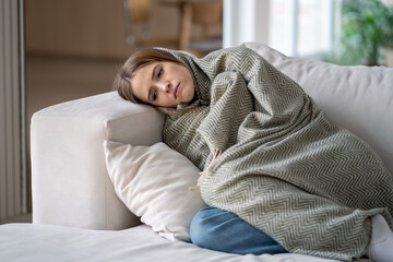 Woman lying on couch covered by blanket, feeling emotionally drained. Depression, loneliness,...