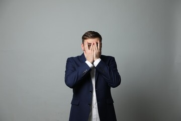 Young businessman feeling fear on grey background