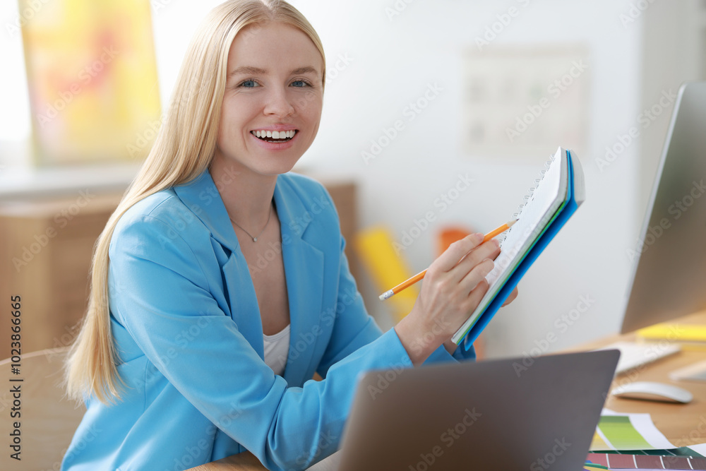 Poster designer with notebook and laptop working at table in office