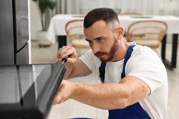 Fototapeta premium Repairman with screwdriver fixing oven at home