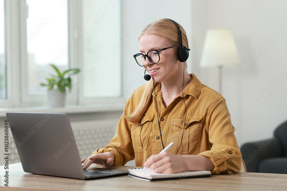 Poster interpreter in headset taking notes while working with laptop at table indoors