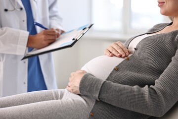 Doctor with clipboard consulting pregnant patient in clinic, closeup