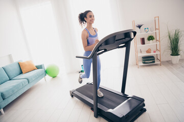 Fototapeta premium Young woman enjoying a treadmill workout in modern home interior with natural light