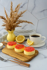 Three cheesecakes topped with red crumble served on a wooden board with a cup of coffee and lemon slices. Concept of cozy breakfast, homemade dessert, and refreshing citrus flavors. High quality photo