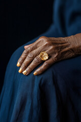 Captivating photography of a senior African American woman's hand wearing a vintage-style gold ring, beautifully contrasted against a dark navy blue background.