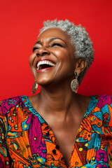 Laughing middle-aged Black woman, in a colorful dress, with a bold red background, showing a natural expression of joy, ready for a profile picture.