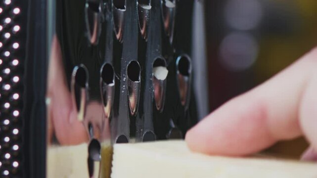 Close-up shot of a hand grating cheese on a grater. Process of grating cheese for culinary use. Coocking at home. 