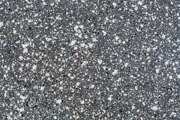 Close-up view of a dark gray asphalt, concrete surface with a speckled texture. Small white and light gray specks on a surface. Abstract background. Design, construction, urban environment concepts. 