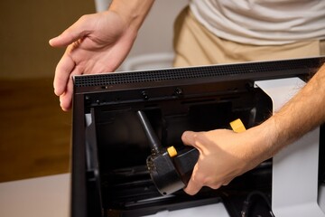 A man cleans a computer case with a vacuum in a bright room, stressing workspace tidiness