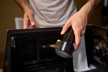 A man cleans a computer case with a vacuum in a bright room, stressing workspace tidiness