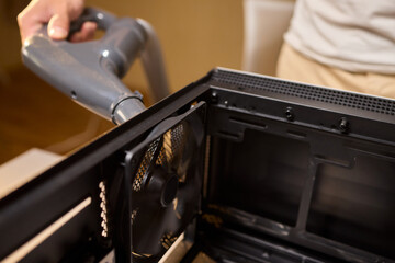 A man cleans a computer case with a vacuum in a bright room, stressing workspace tidiness