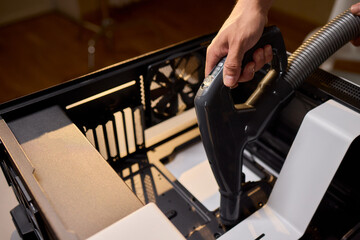 A man cleans a computer case with a vacuum in a bright room, stressing workspace tidiness