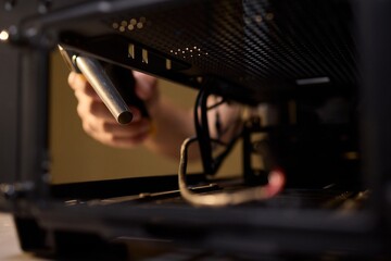 A man cleans a computer case with a vacuum in a bright room, stressing workspace tidiness