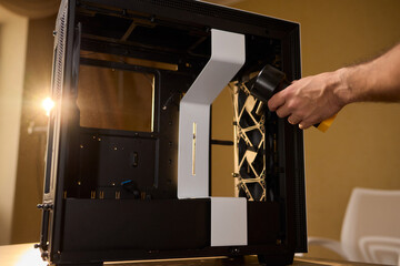 A man cleans a computer case with a vacuum in a bright room, stressing workspace tidiness