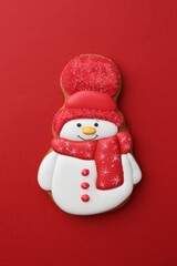 Tasty Christmas cookie in shape of snowman on red background, top view