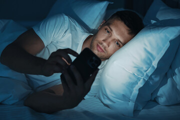 Fototapeta premium Bad habit. Man using smartphone in bed at night
